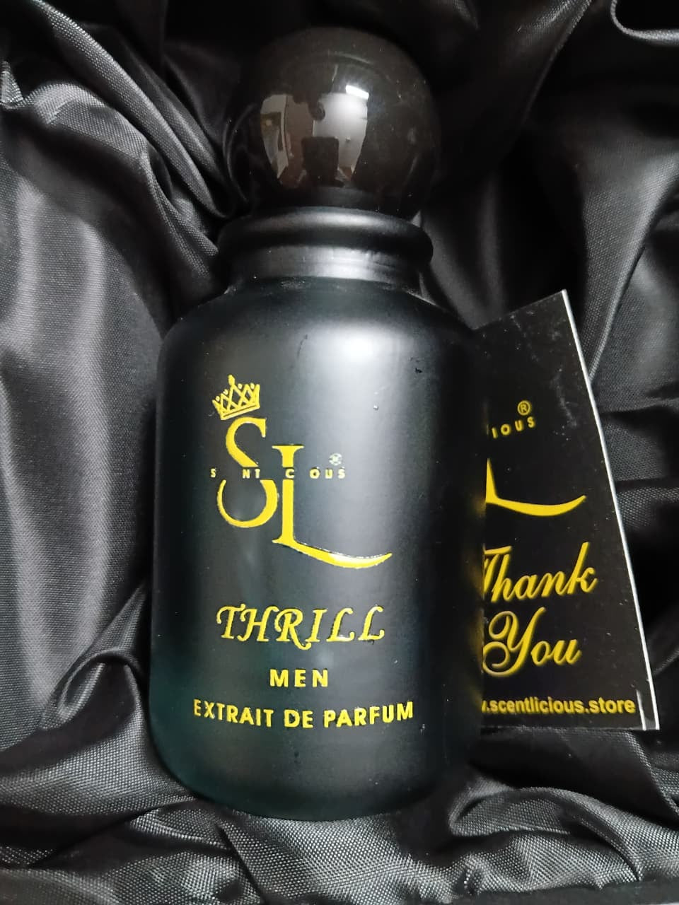 Black perfume bottle with yellow text on a black satin background